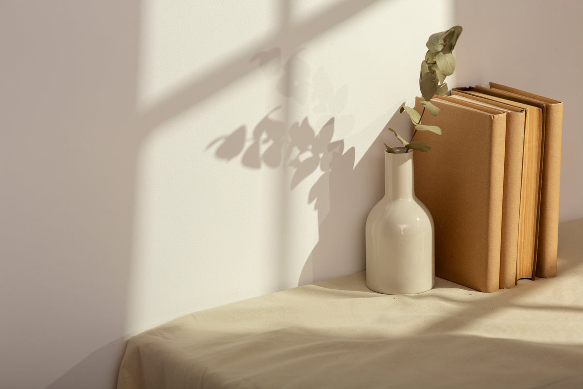 A ceramic vase and neutral books in warm afternoon sunlight